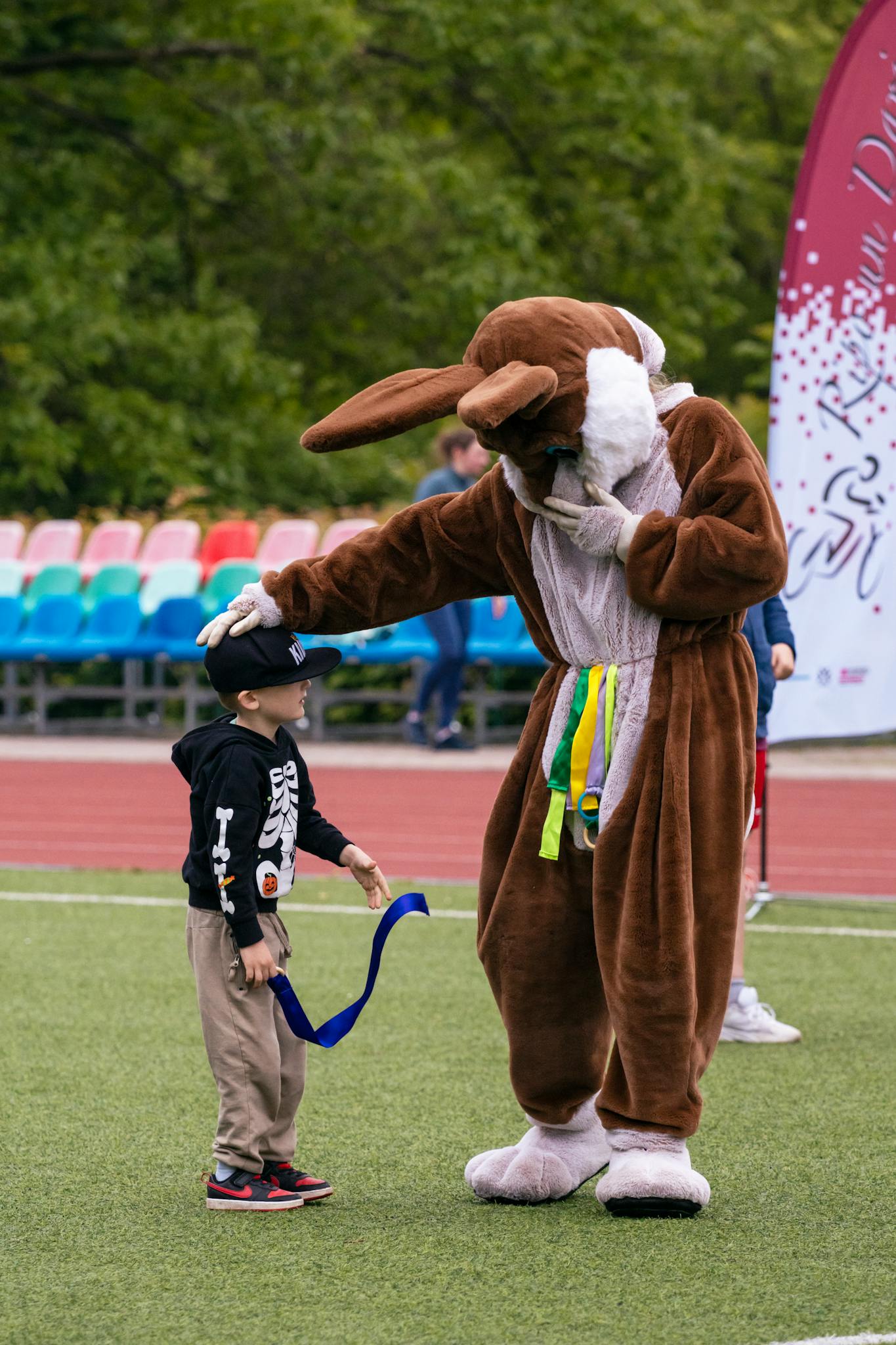 A child receives an award from a bunny mascot during a fun outdoor event on a sports field.